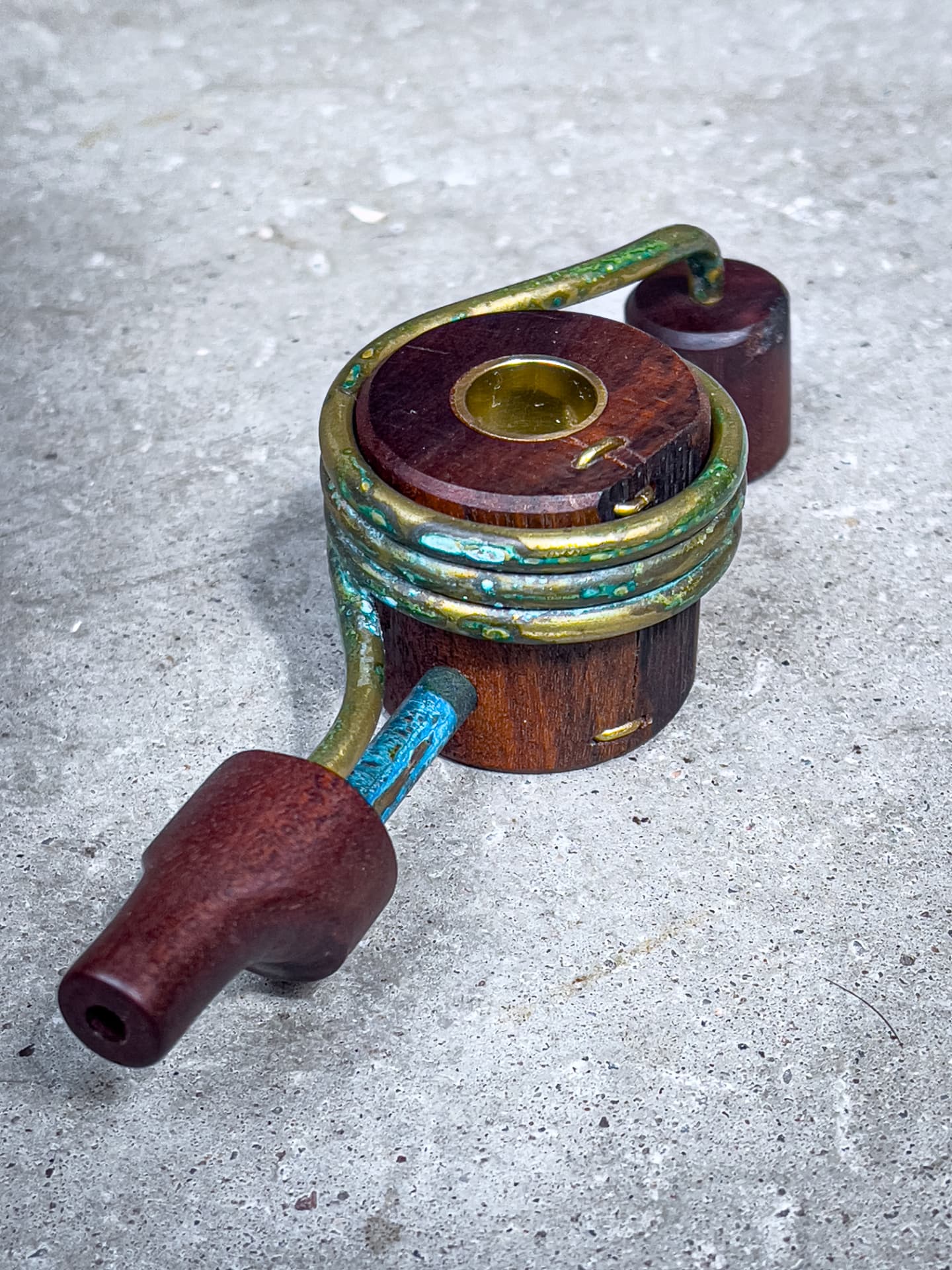 Custom Ancient Pothead pipe with a patinated brass coil and wooden mouthpiece on a concrete surface